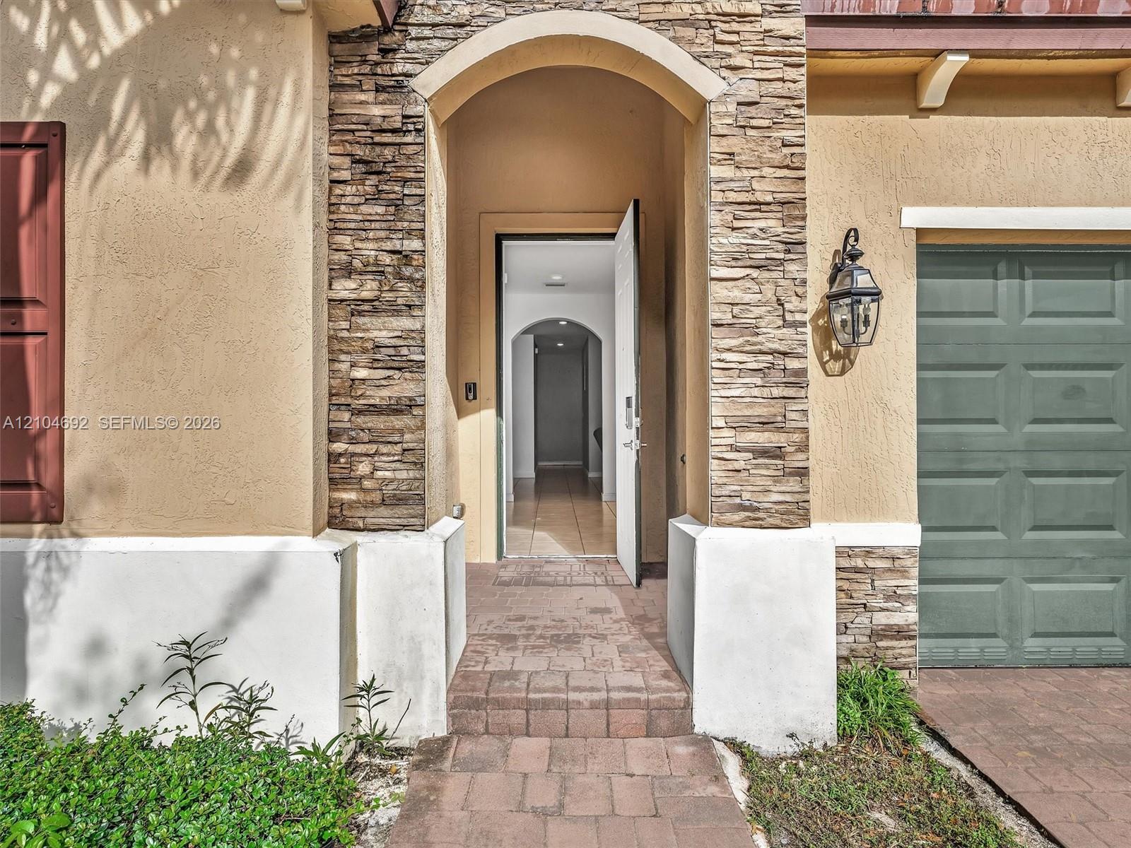 Stucco exterior featuring stacked stone accents, an arched entryway, paver walkway, and a carriage-style garage door with an attached wall-mounted lantern Stucco exterior featuring stacked stone accents, an arched entryway, paver walkway, and a carriage-style garage door with an attached wall-mounted lantern