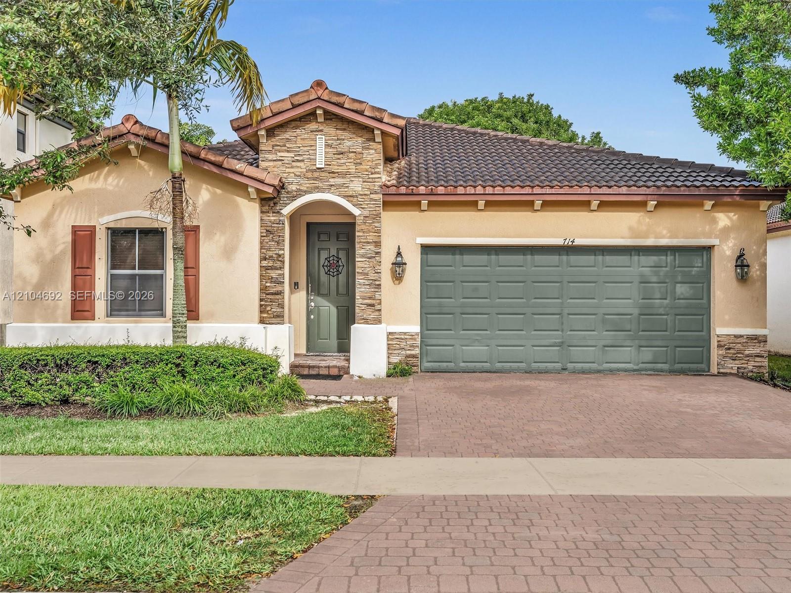 Stucco exterior featuring stacked stone accents, tile roof, decorative shutters, and a paved driveway