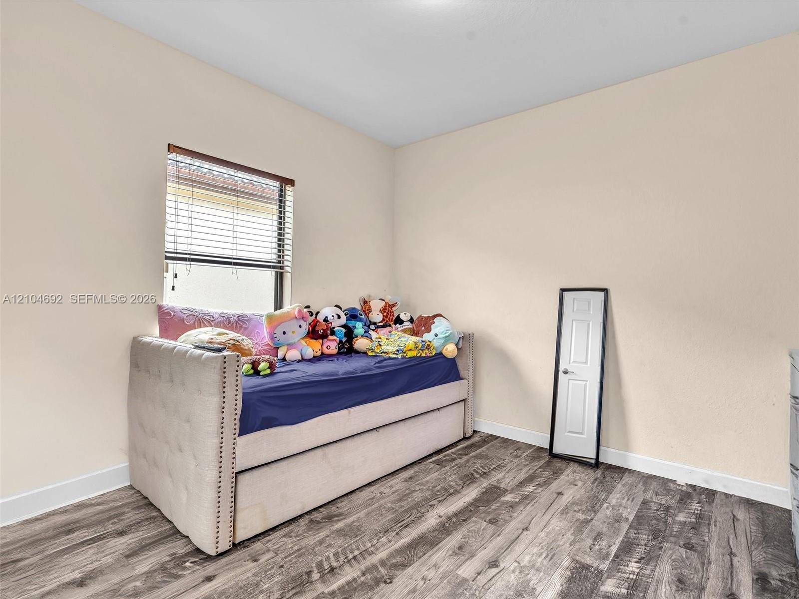 Room interior featuring wood-finish flooring, neutral wall paint, and a window with horizontal blinds