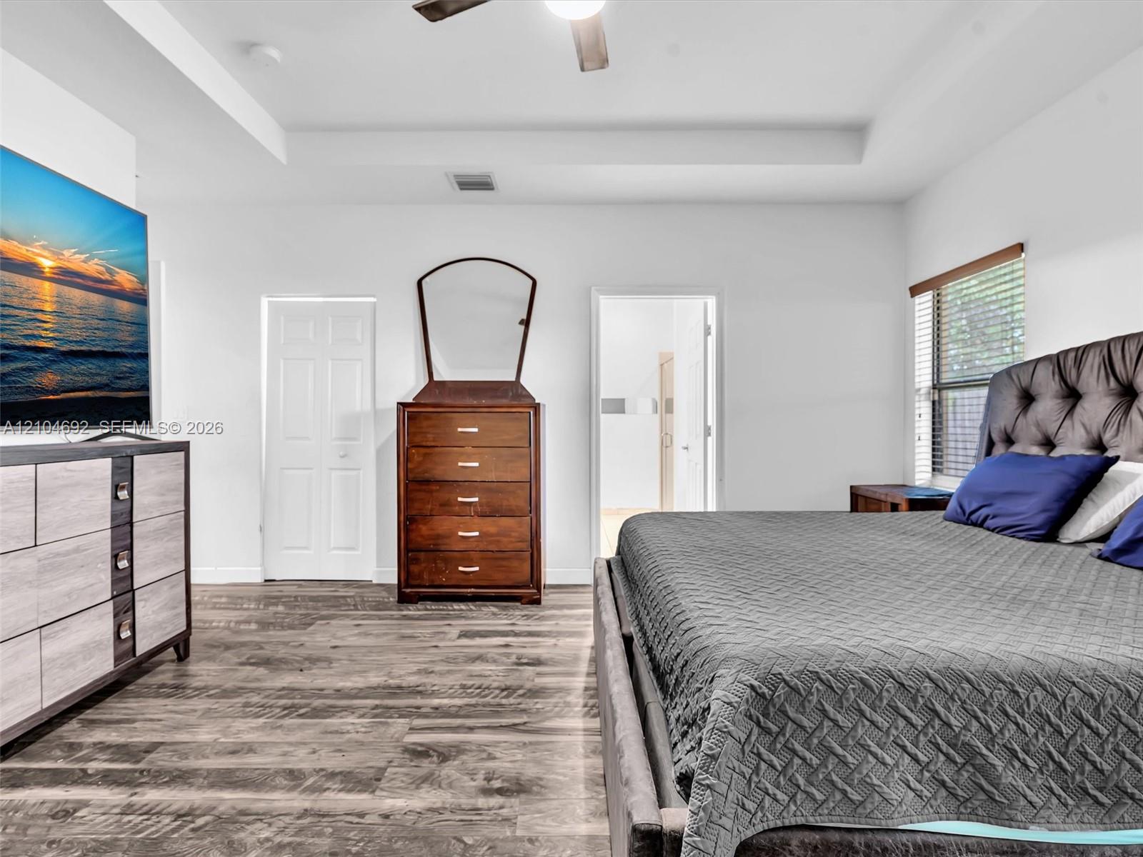 Tray ceiling with an integrated ceiling fan, wood-finish flooring, and window blinds