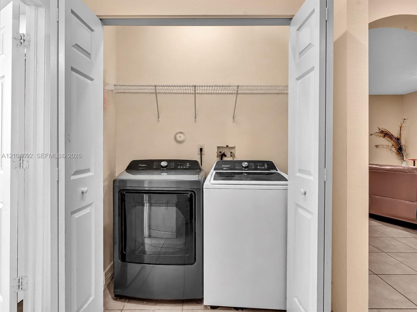 Laundry area featuring bi-fold doors, white ceramic tile flooring, and integrated wire shelving Laundry area featuring bi-fold doors, white ceramic tile flooring, and integrated wire shelving