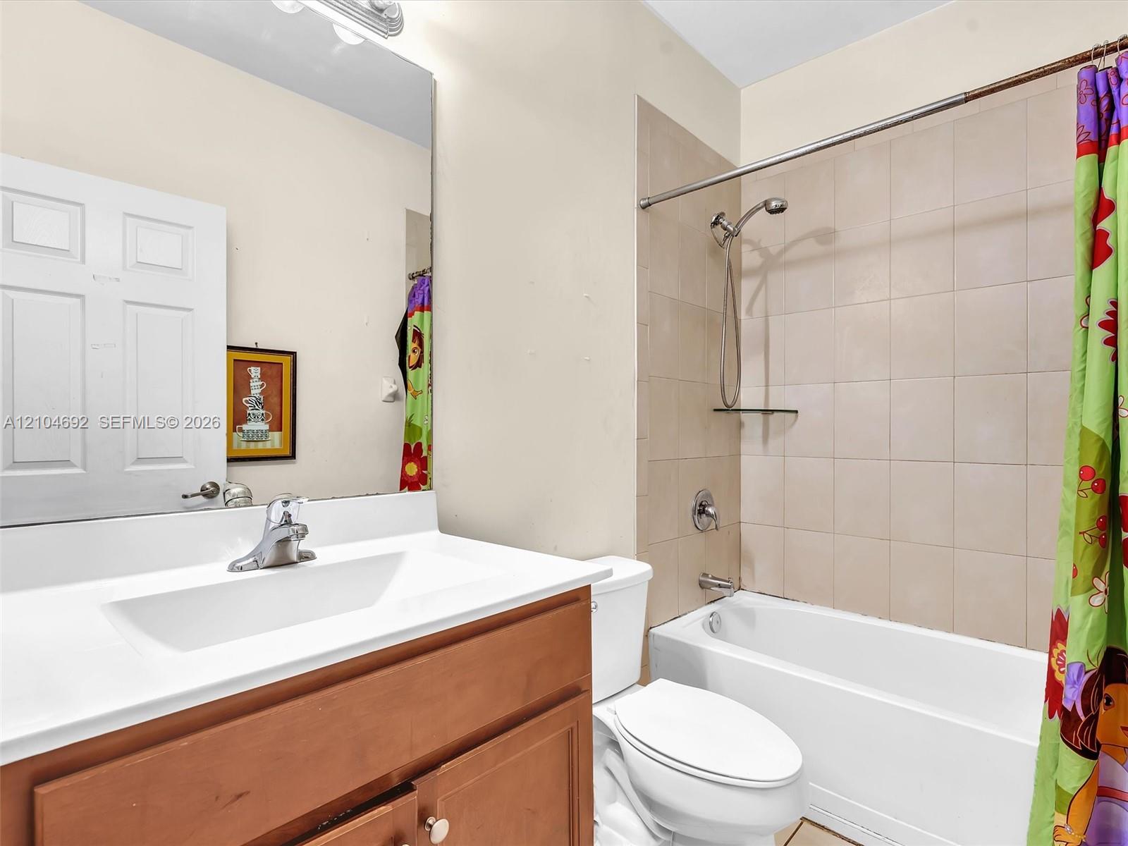 Bathroom featuring a wood-finish vanity with a white countertop, large wall-mounted mirror, and a tile-surround shower and tub combination with a detachable showerhead