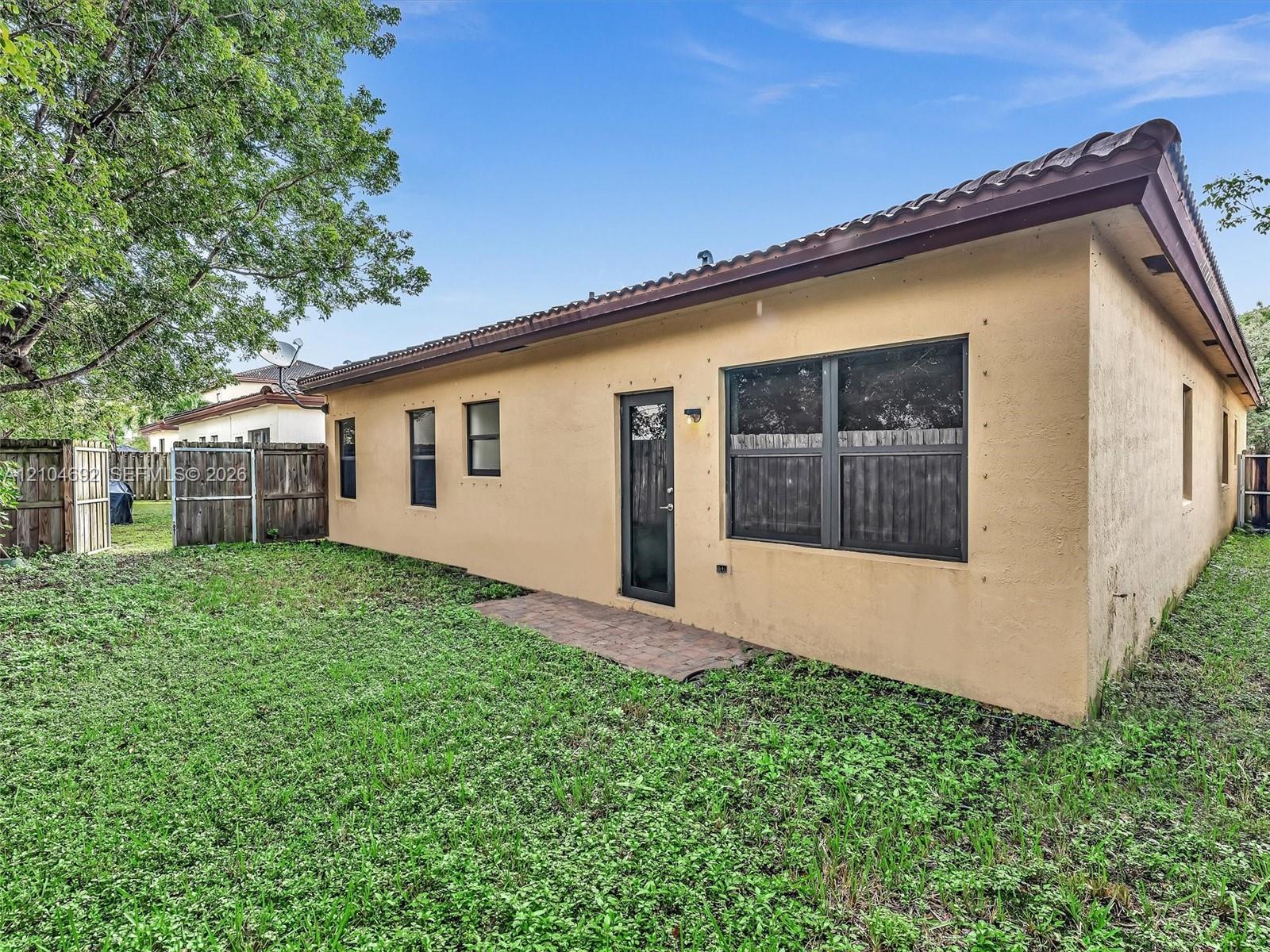Stucco exterior featuring a tile roof, paved rear patio, single-light glass door, and wooden perimeter fencing