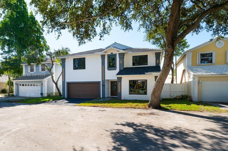 Two-story exterior featuring a light-toned stucco faade, decorative column detailing, a multi-paneled garage door, and a shingle roof Two-story exterior featuring a light-toned stucco faade, decorative column detailing, a multi-paneled garage door, and a shingle roof