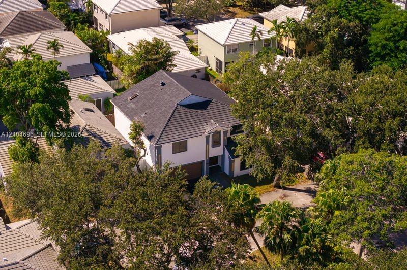 Aerial perspective of a multi-story residence featuring a shingled hipped roof, light-toned exterior finish, attached garage, and mature tree canopy throughout the parcel