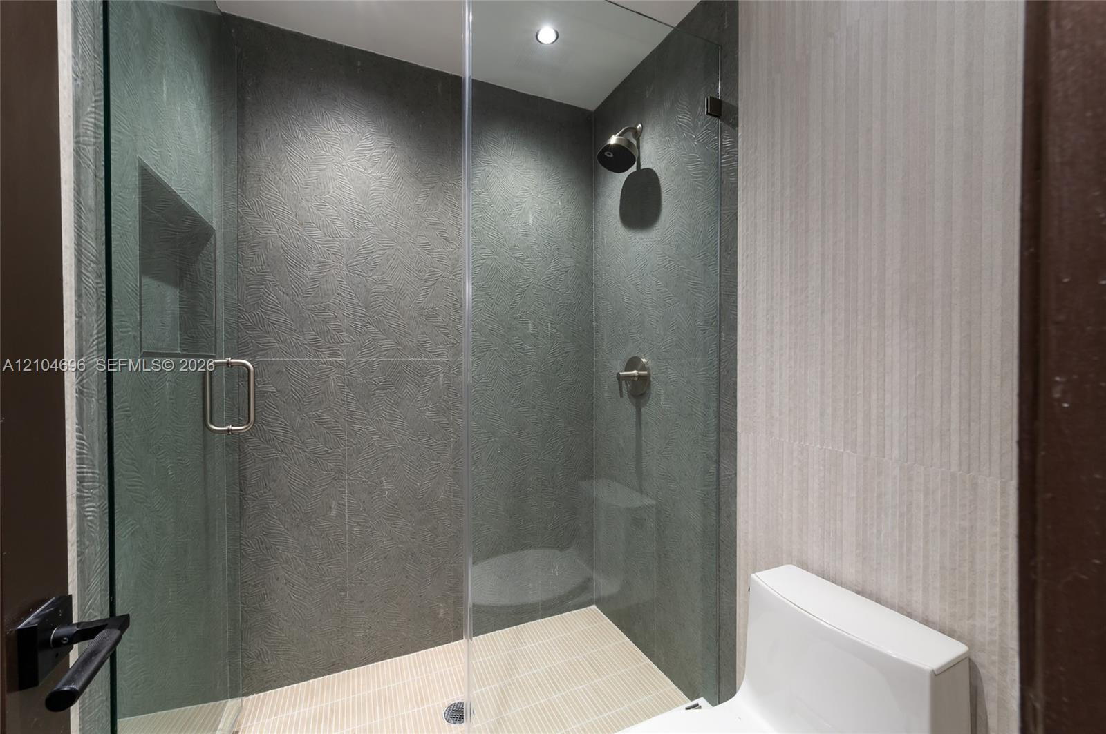 Walk-in shower featuring textured dark stone-style wall tile, frameless glass enclosure, built-in recessed wall niche, and integrated rainfall showerhead