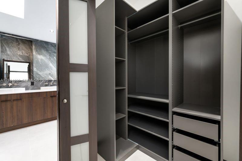 Custom built-in dark finish closet shelving with integrated drawers and hanging rods, featuring a sliding door with frosted glass panels, wood-finish cabinetry, and stone-surround wall tiling