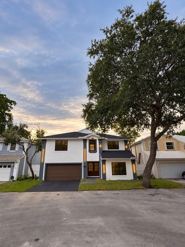 Two-story residence featuring a painted brick facade, dark-toned roof shingles, a multi-car garage, and linear exterior wall lighting Two-story residence featuring a painted brick facade, dark-toned roof shingles, a multi-car garage, and linear exterior wall lighting