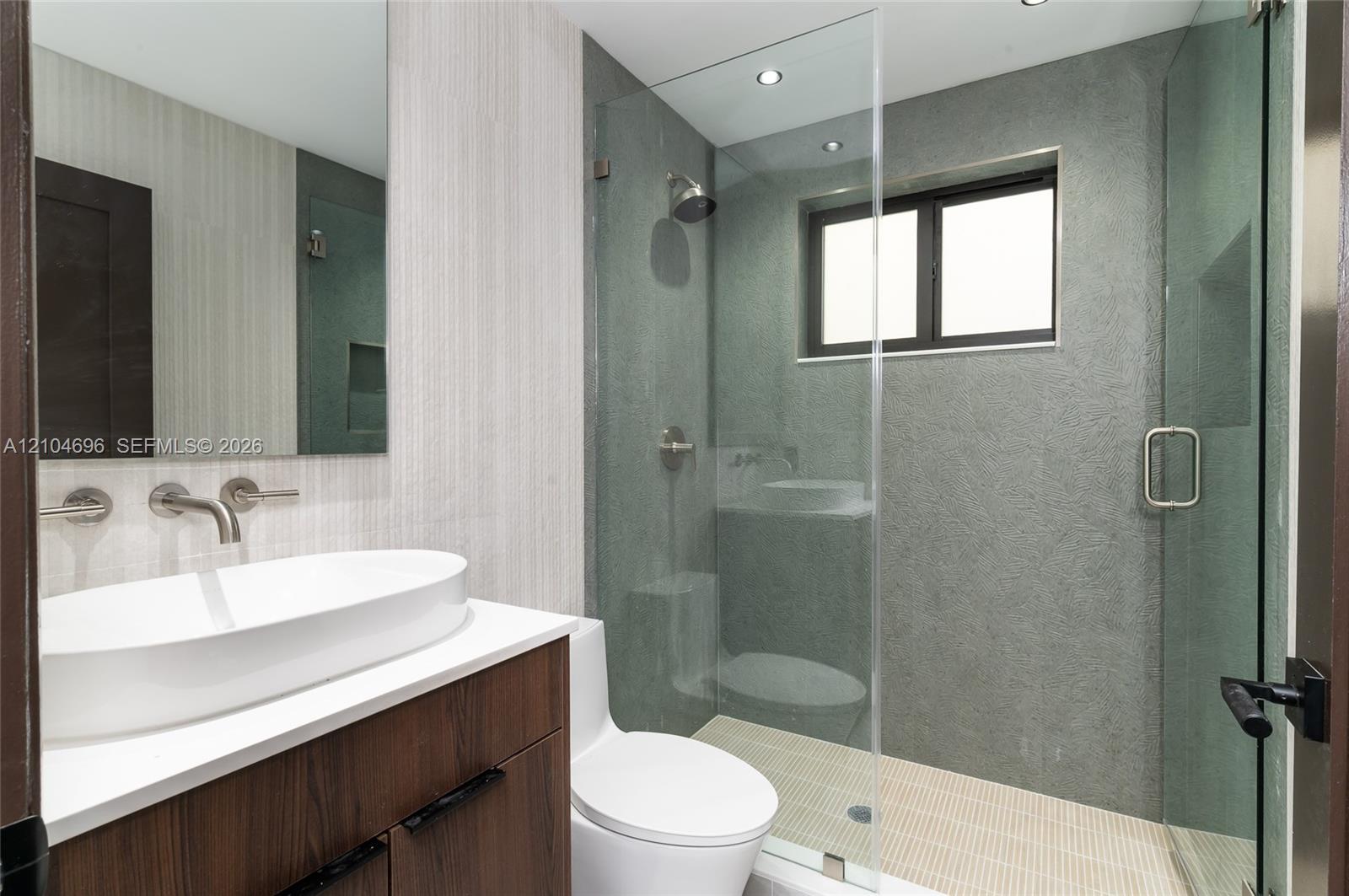 Modern bathroom featuring a wood-finish floating vanity with a white vessel sink, quartz countertop, wall-mounted faucet, and a glass-enclosed shower with textured grey tile surrounds