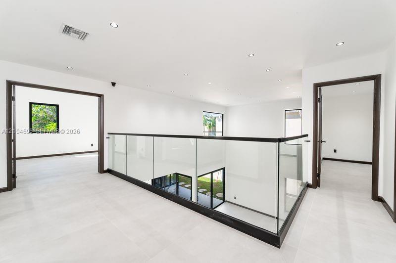 Open-concept landing featuring glass railings with dark metal trim, large-format tile flooring, and recessed ceiling lighting