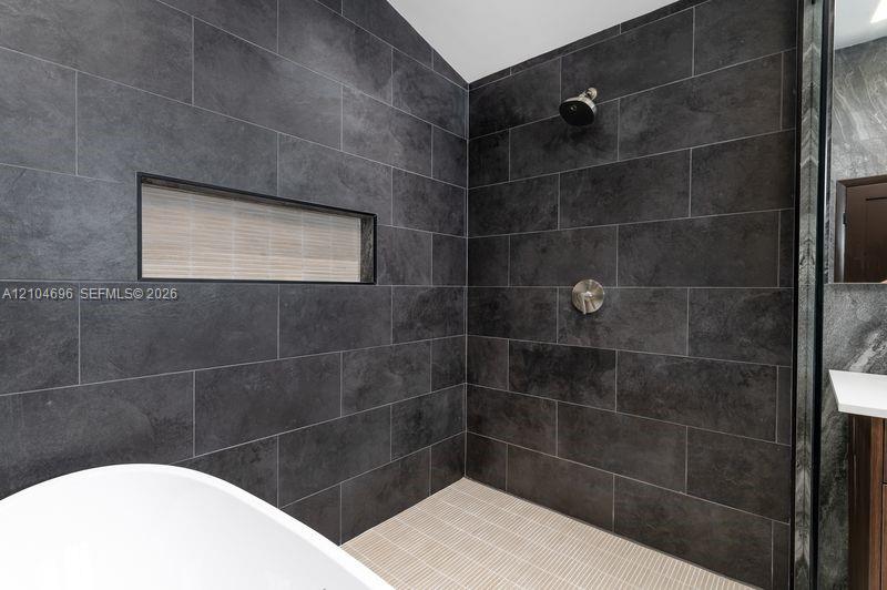 Walk-in shower with dark large-format tile surround, integrated horizontal niche, fixed shower head, and neutral grid-patterned floor tile