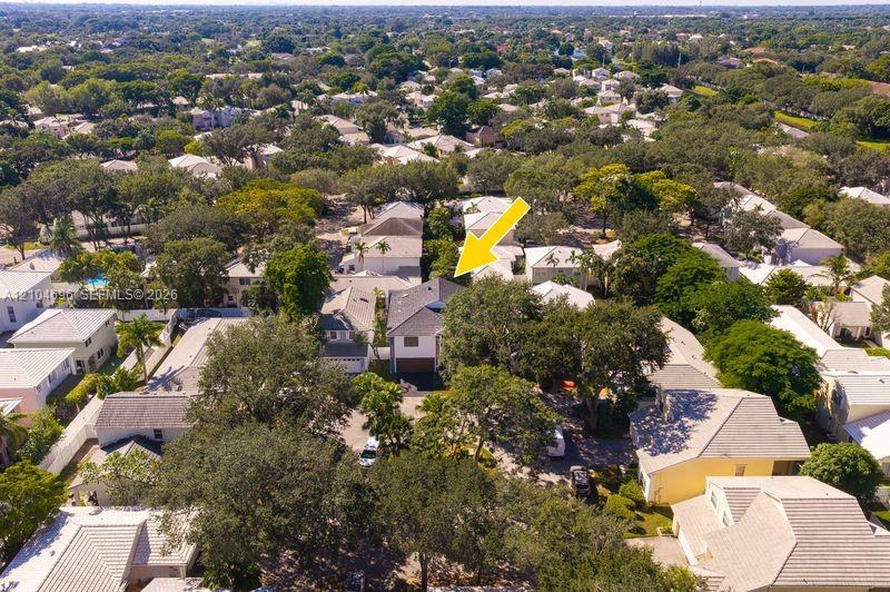 Aerial perspective featuring a two-story residence with a multi-hipped roof, paved driveway, attached garage, and mature tree canopy