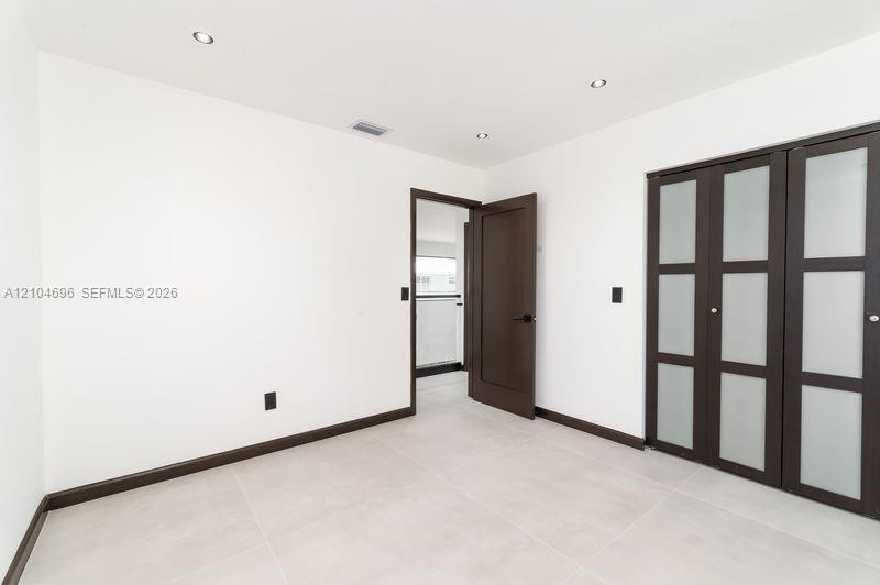 Interior space featuring light-toned tile flooring, recessed ceiling lighting, a dark-finish interior door, and a built-in closet with frosted glass panels