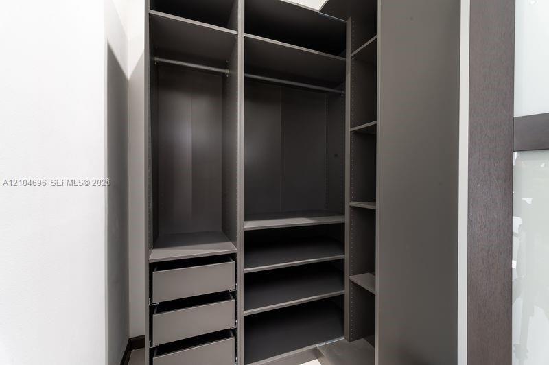 Custom storage system featuring dark wood-finish cabinetry, integrated shelving, tiered drawer units, and metal garment rods