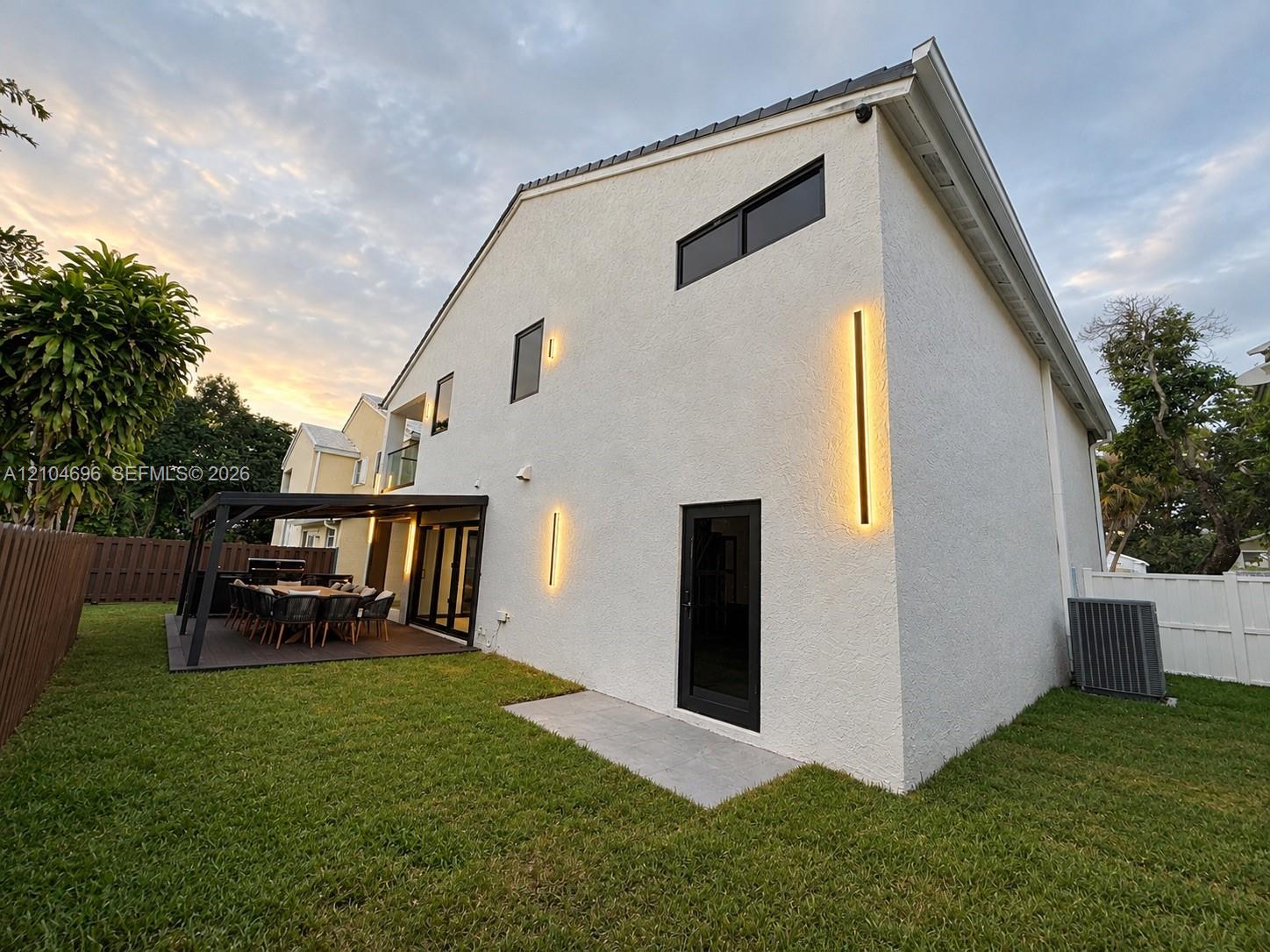 Stucco exterior featuring vertical linear wall sconces, a covered patio with dark-finish decking, and black-trimmed windows and doors