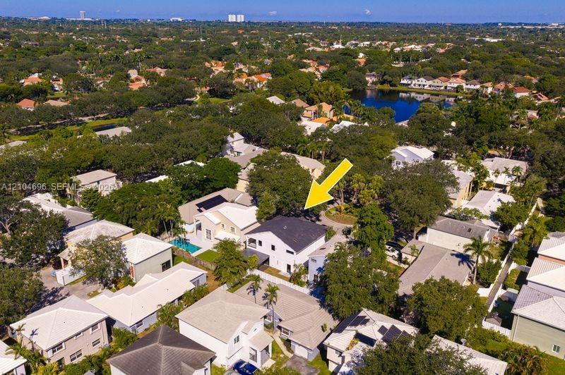 Aerial perspective featuring a two-story residence with a dark shingle roof, integrated pool, and mature canopy trees on a landscaped lot