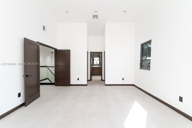 High-ceilinged room featuring large-format tile flooring, dark-toned interior doors, recessed lighting, and expansive window with dark framing