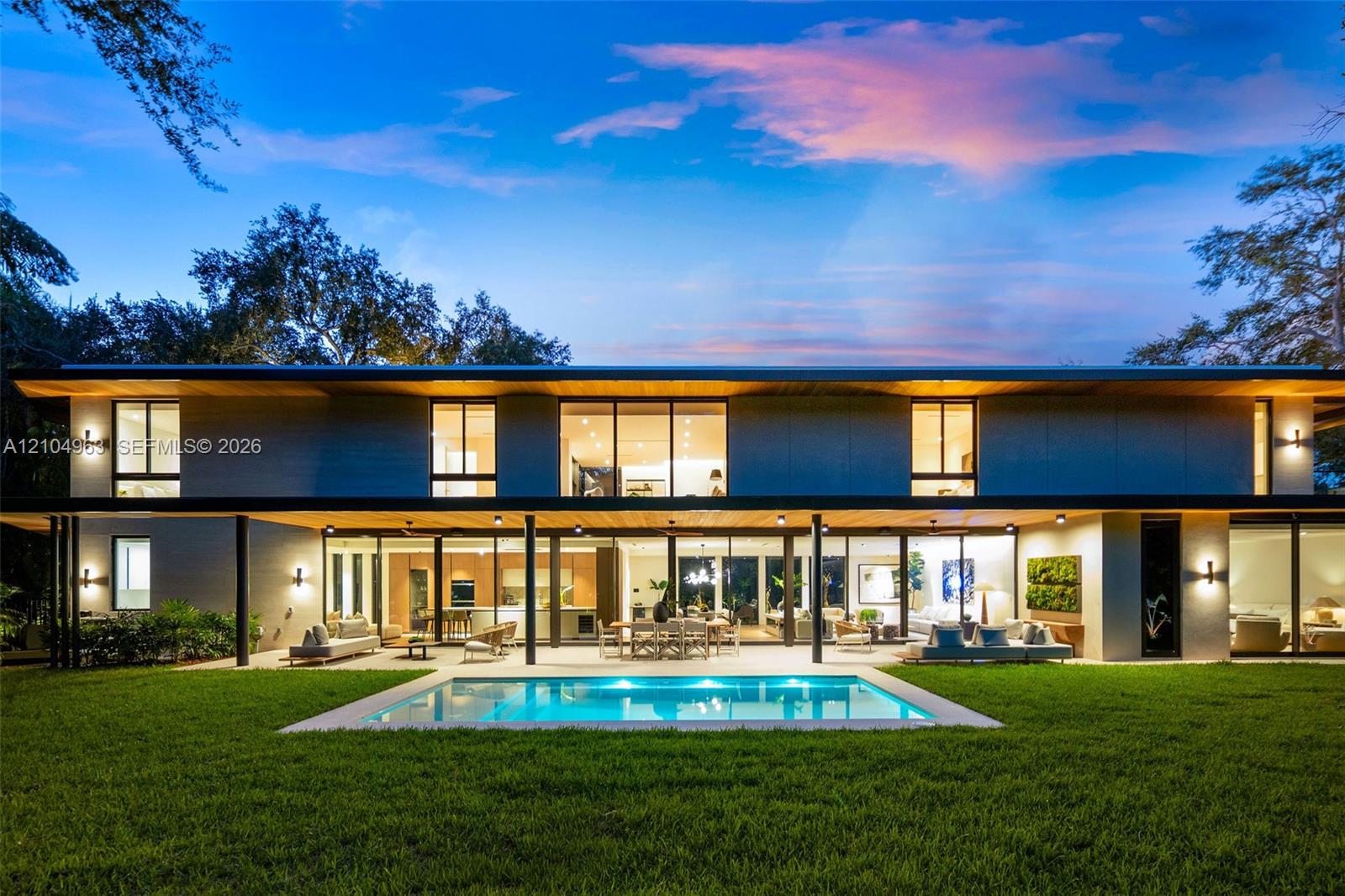 Modern two-story architectural exterior featuring expansive glass walls, a covered patio with recessed lighting, a rectangular in-ground pool, and wood-finish ceiling accents Modern two-story architectural exterior featuring expansive glass walls, a covered patio with recessed lighting, a rectangular in-ground pool, and wood-finish ceiling accents