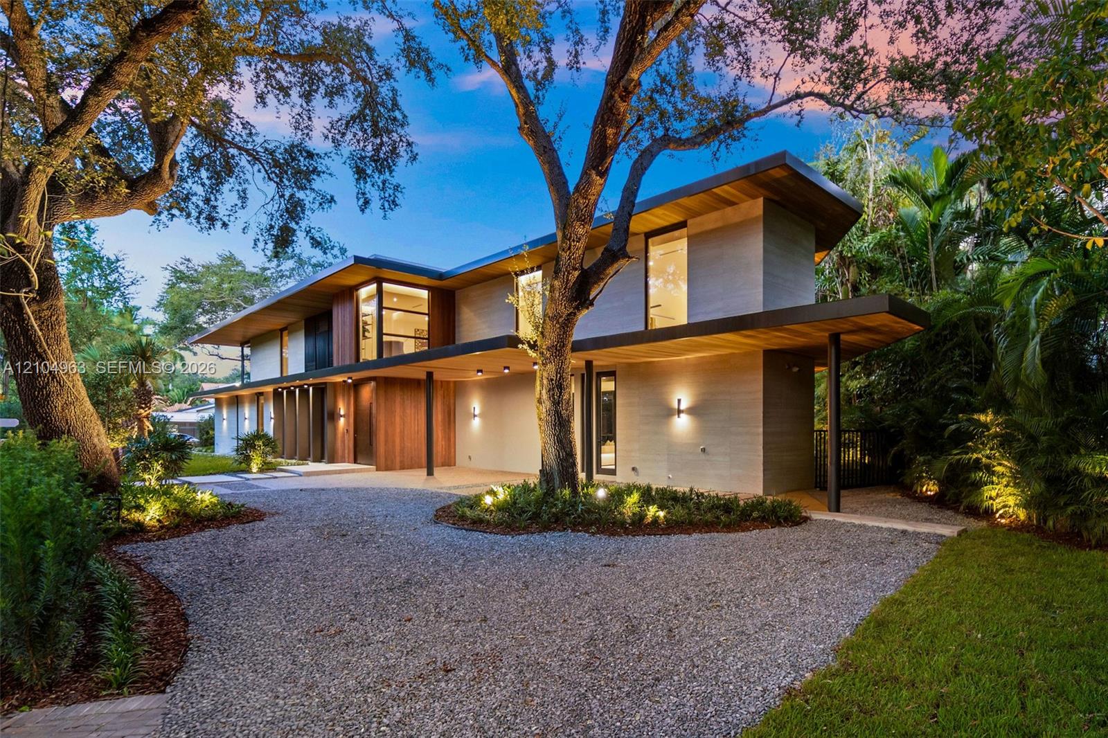 Modern architectural exterior featuring horizontal wood siding, expansive glass windows, flat roofline with extended overhangs, and a gravel driveway