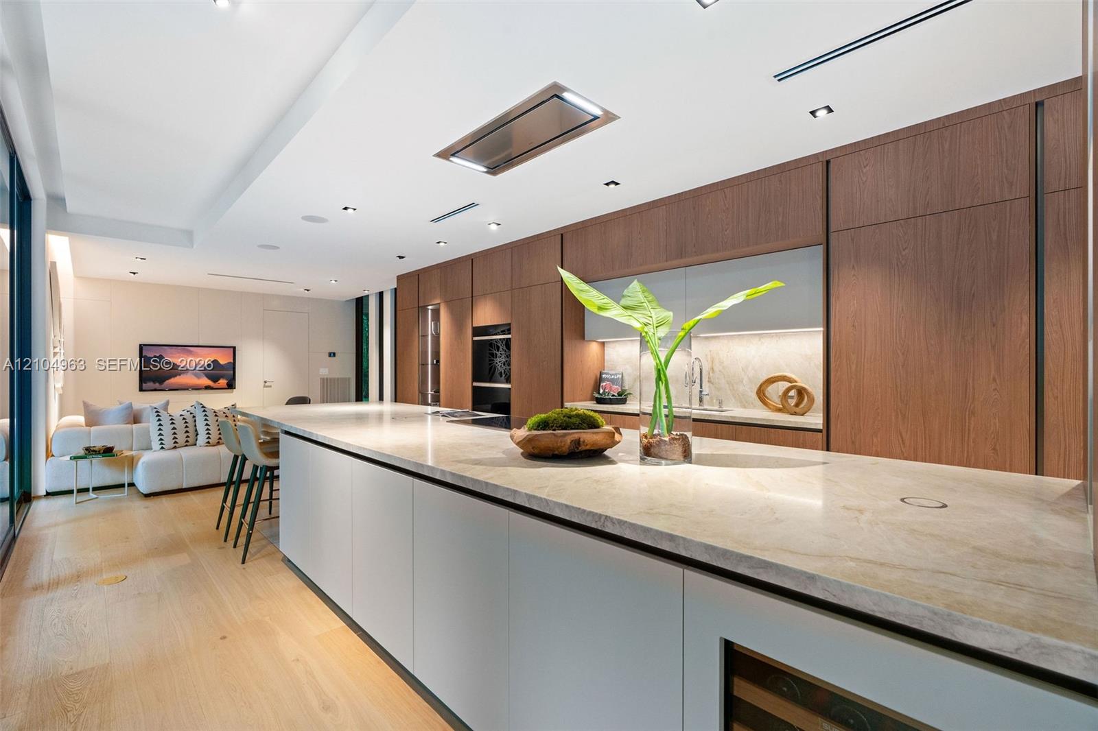 Kitchen featuring full-height wood-finish cabinetry, a lengthy stone-surfaced island, integrated double wall ovens, a built-in wine refrigerator, and light wood-finish flooring