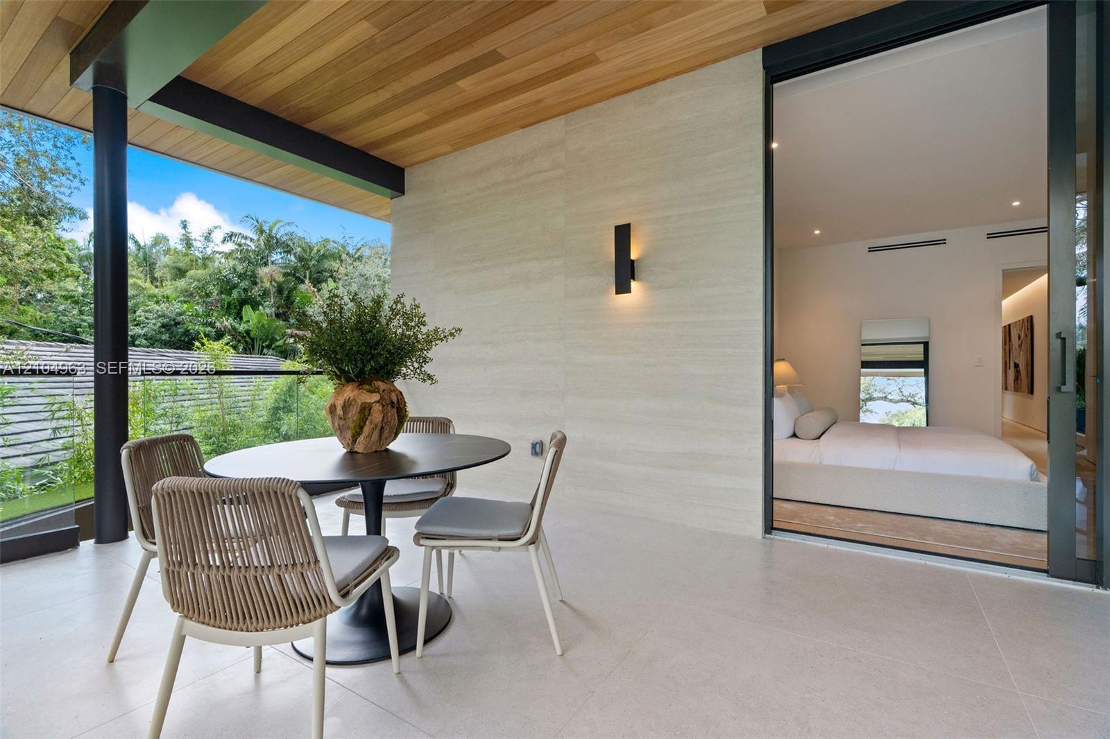 Covered balcony featuring wood-paneled ceiling, stone-finish wall cladding, large-format tile flooring, frameless glass railings, and expansive sliding glass doors