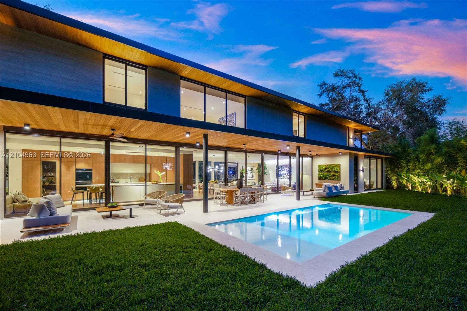Modern two-story exterior featuring expansive floor-to-ceiling glass wall systems, a recessed wood-paneled ceiling, a rectangular in-ground swimming pool, and stone pool decking Modern two-story exterior featuring expansive floor-to-ceiling glass wall systems, a recessed wood-paneled ceiling, a rectangular in-ground swimming pool, and stone pool decking