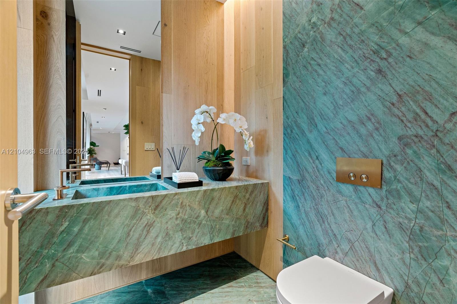 Floating vanity with integrated basin, teal stone wall cladding, floor-to-ceiling wood paneling, wall-mounted metallic flush actuator, and recessed ceiling lighting
