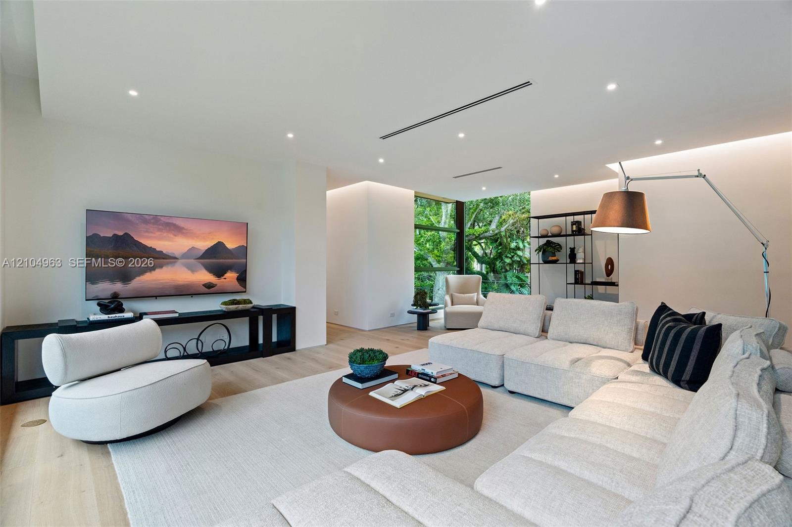 Wide-plank wood-finish flooring, recessed ceiling lighting, linear slot diffusers, and floor-to-ceiling windows featuring exterior greenery