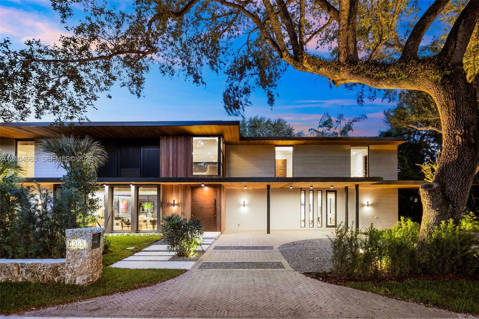 Modern multi-level exterior featuring wood-paneled siding, stone-finished masonry, expansive floor-to-ceiling glass windows, and a paved herringbone driveway Modern multi-level exterior featuring wood-paneled siding, stone-finished masonry, expansive floor-to-ceiling glass windows, and a paved herringbone driveway