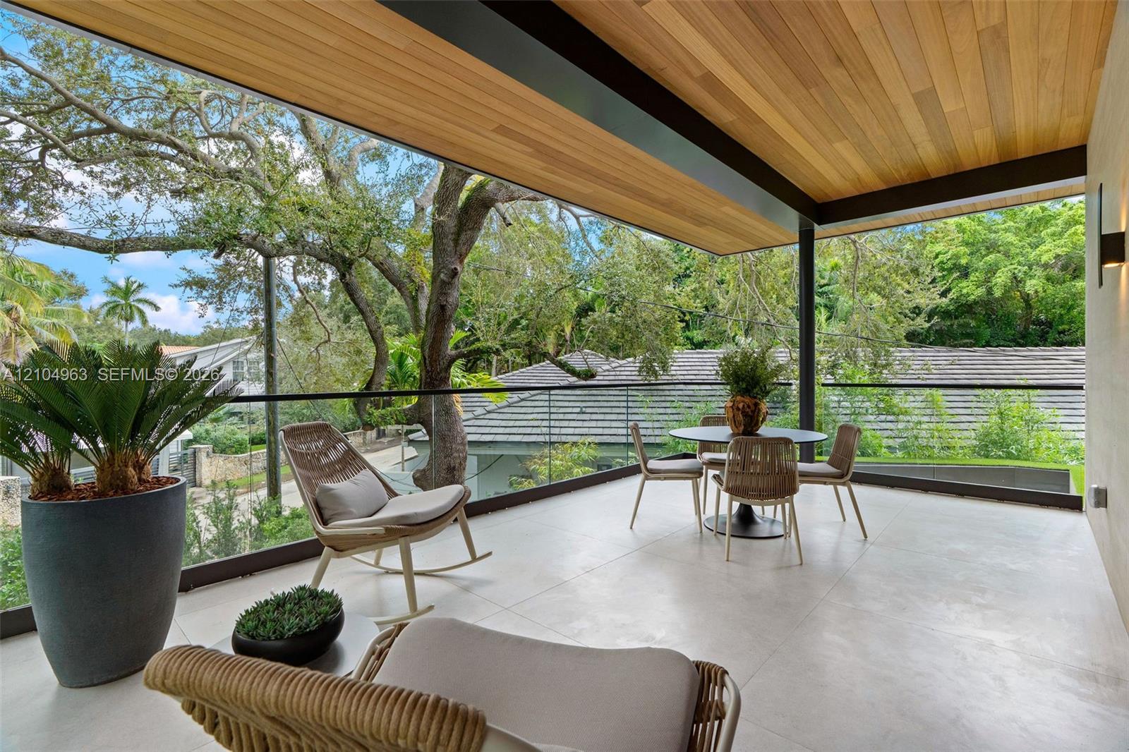 Covered balcony featuring wood-plank ceiling finish, large-format tile flooring, and a frameless glass railing system