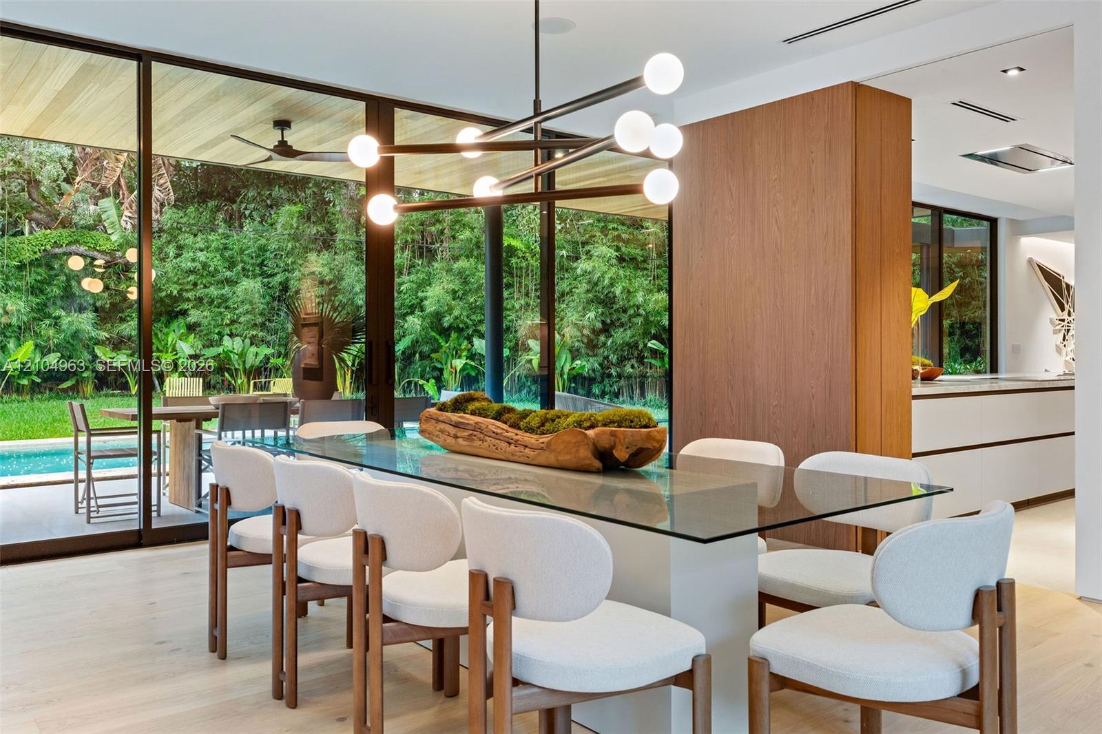 Floor-to-ceiling glass walls, wood-finish flooring, architectural multi-bulb chandelier, and wood-paneled feature wall