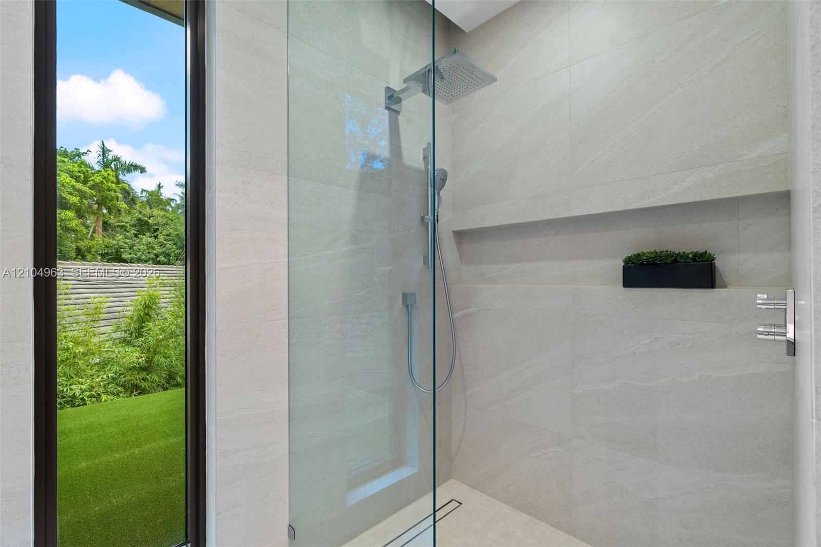 Walk-in shower featuring floor-to-ceiling stone-finish tile, frameless glass enclosure, rainfall shower head, handheld sprayer, and an integrated recessed storage niche