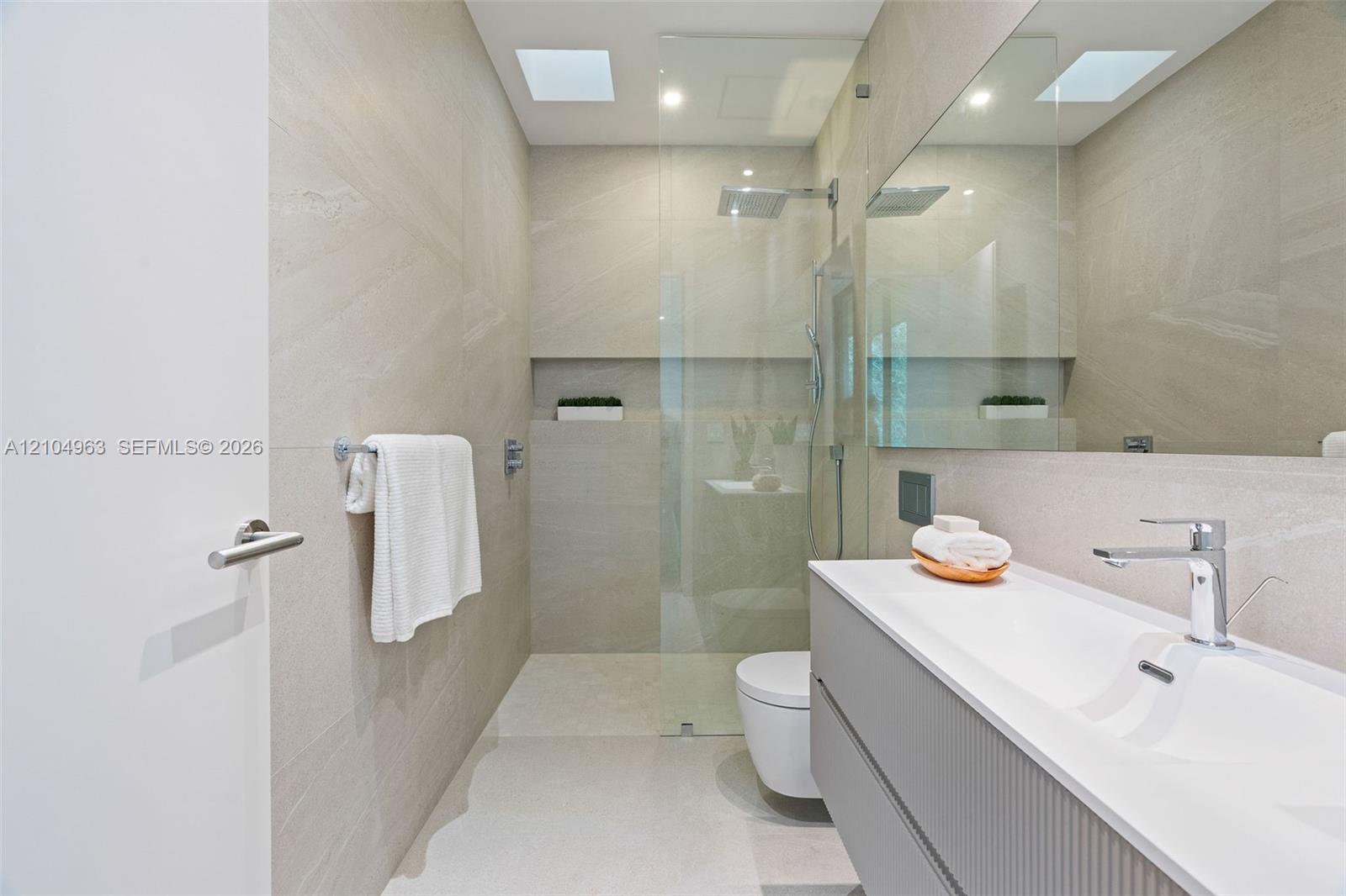 Modern bathroom featuring floor-to-ceiling textured wall tiling, a floating vanity with a seamless integrated sink, a glass-enclosed shower with a built-in recessed wall niche, and a large wall-to-wall mirror