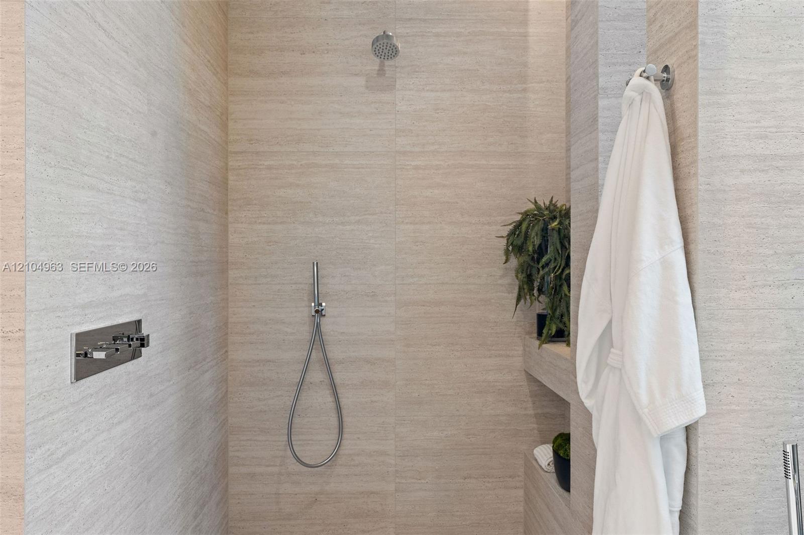 Walk-in shower featuring large-format textured stone wall tile, built-in shelving, a rainfall showerhead, and a wall-mounted handheld shower fixture with chrome hardware