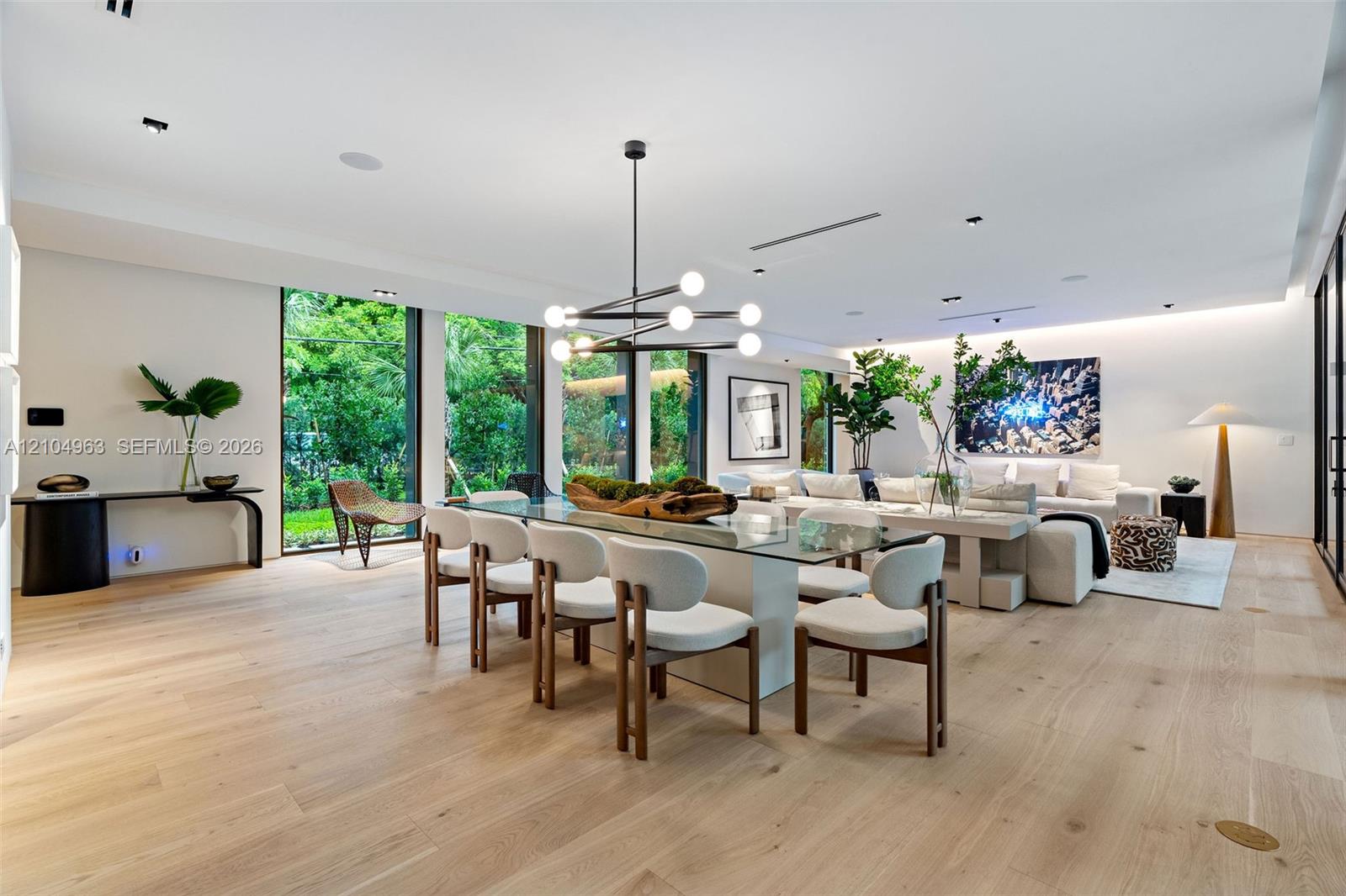Open-concept living space featuring wood-finish flooring, floor-to-ceiling windows, recessed lighting, and a modern tiered geometric chandelier Open-concept living space featuring wood-finish flooring, floor-to-ceiling windows, recessed lighting, and a modern tiered geometric chandelier