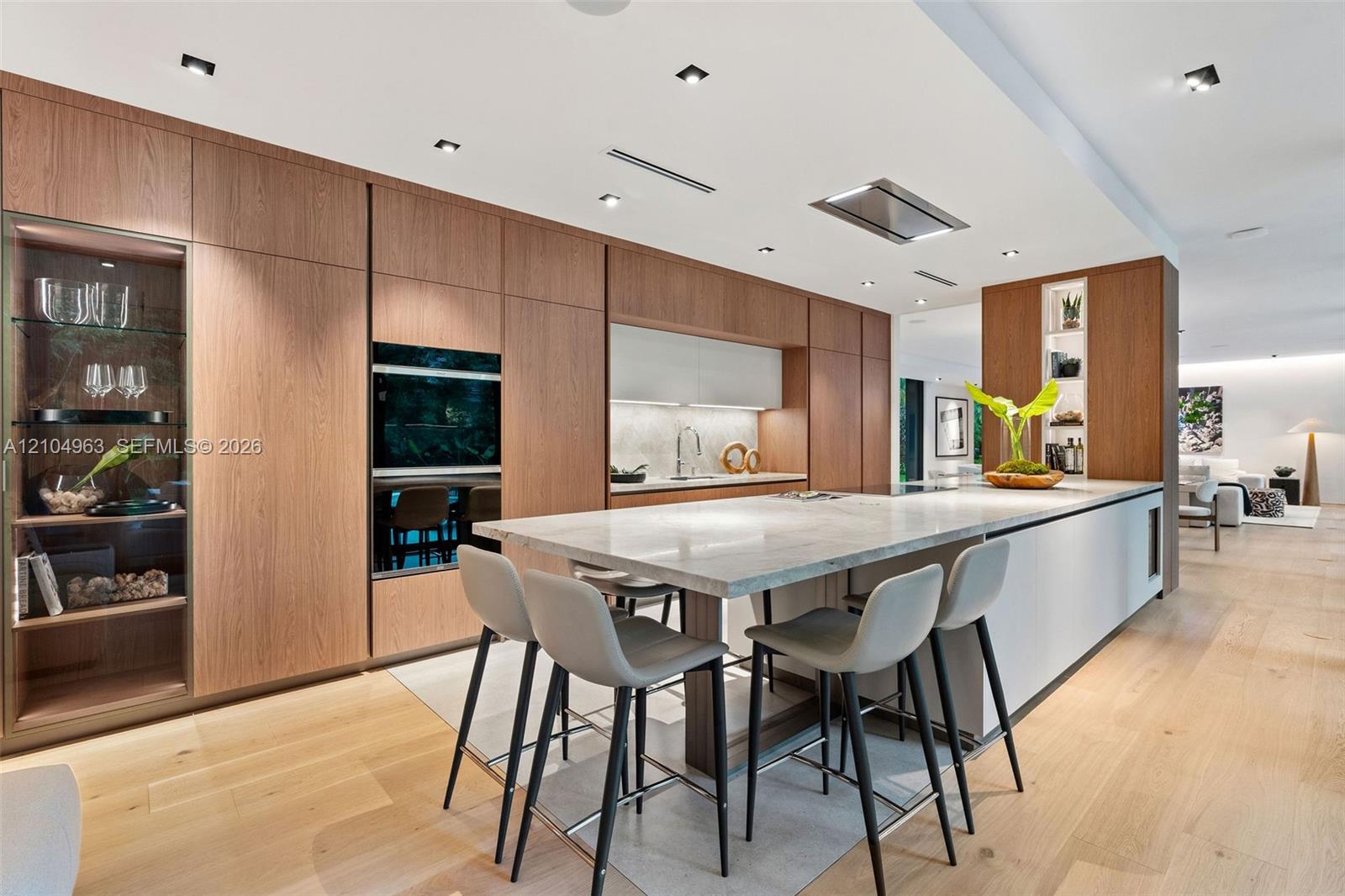 Kitchen featuring flat-panel wood cabinetry, integrated stainless steel double wall ovens, a stone-topped island with waterfall edge, and wood-finish flooring