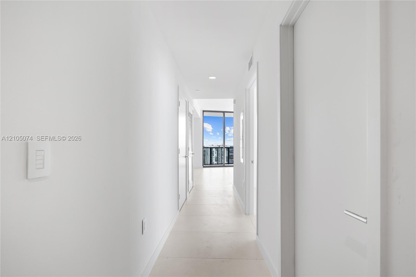 Hallway featuring neutral-toned tile flooring, recessed ceiling lighting, and floor-to-ceiling glass sliding doors