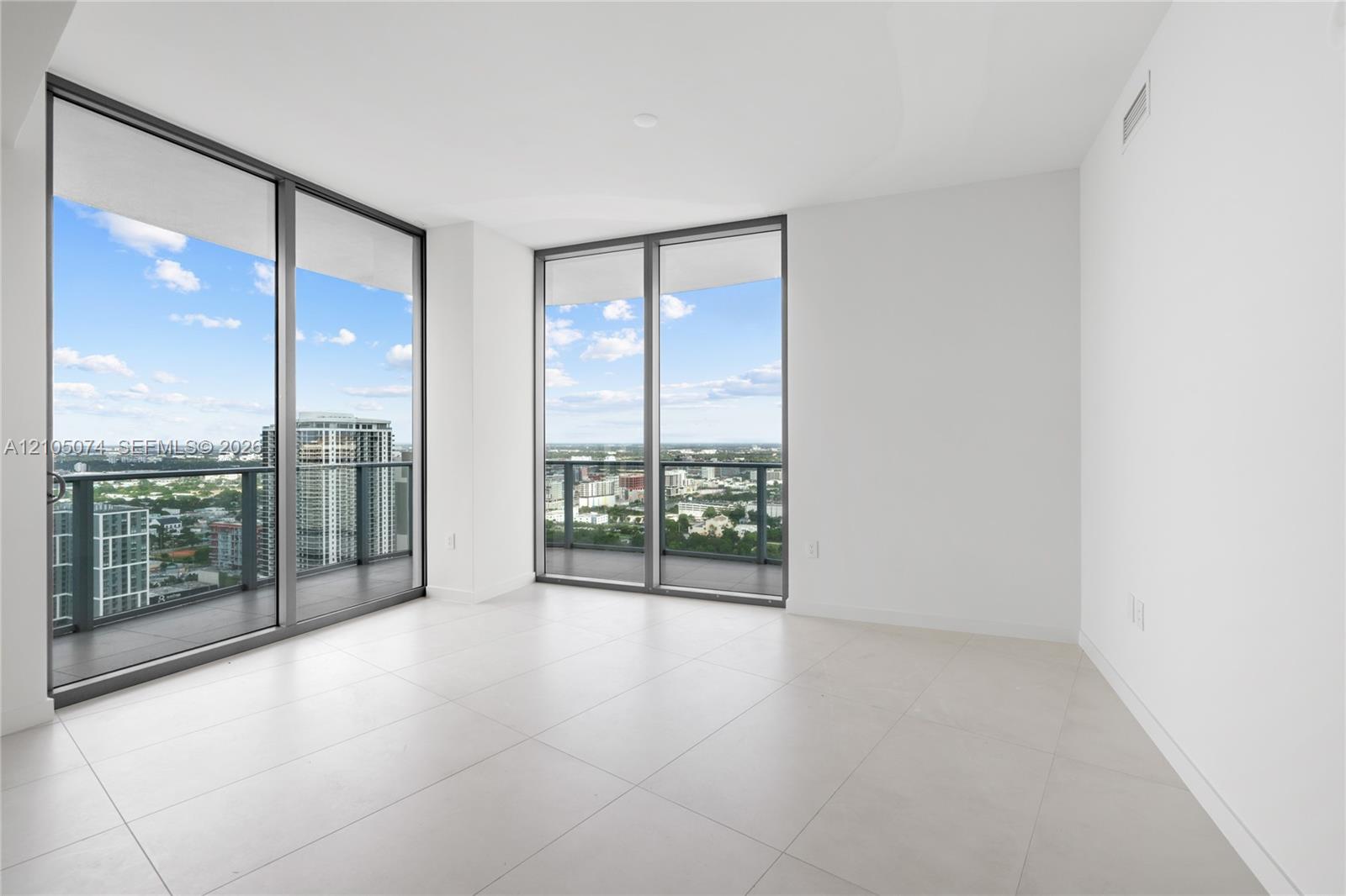 Floor-to-ceiling glass walls, large-format tile flooring, and sliding doors opening to an expansive wrap-around balcony with extensive city scenery