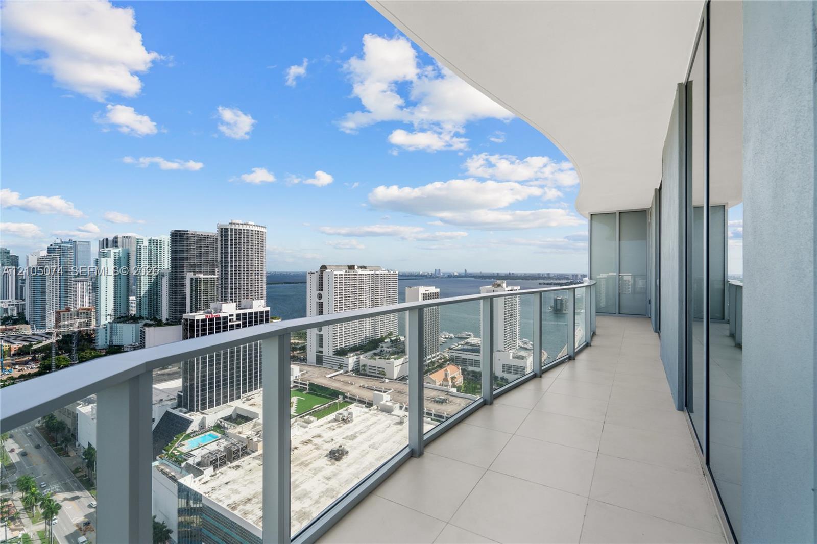 Wraparound balcony featuring large-format tile flooring, a glass panel railing, and full-height glass sliding door access