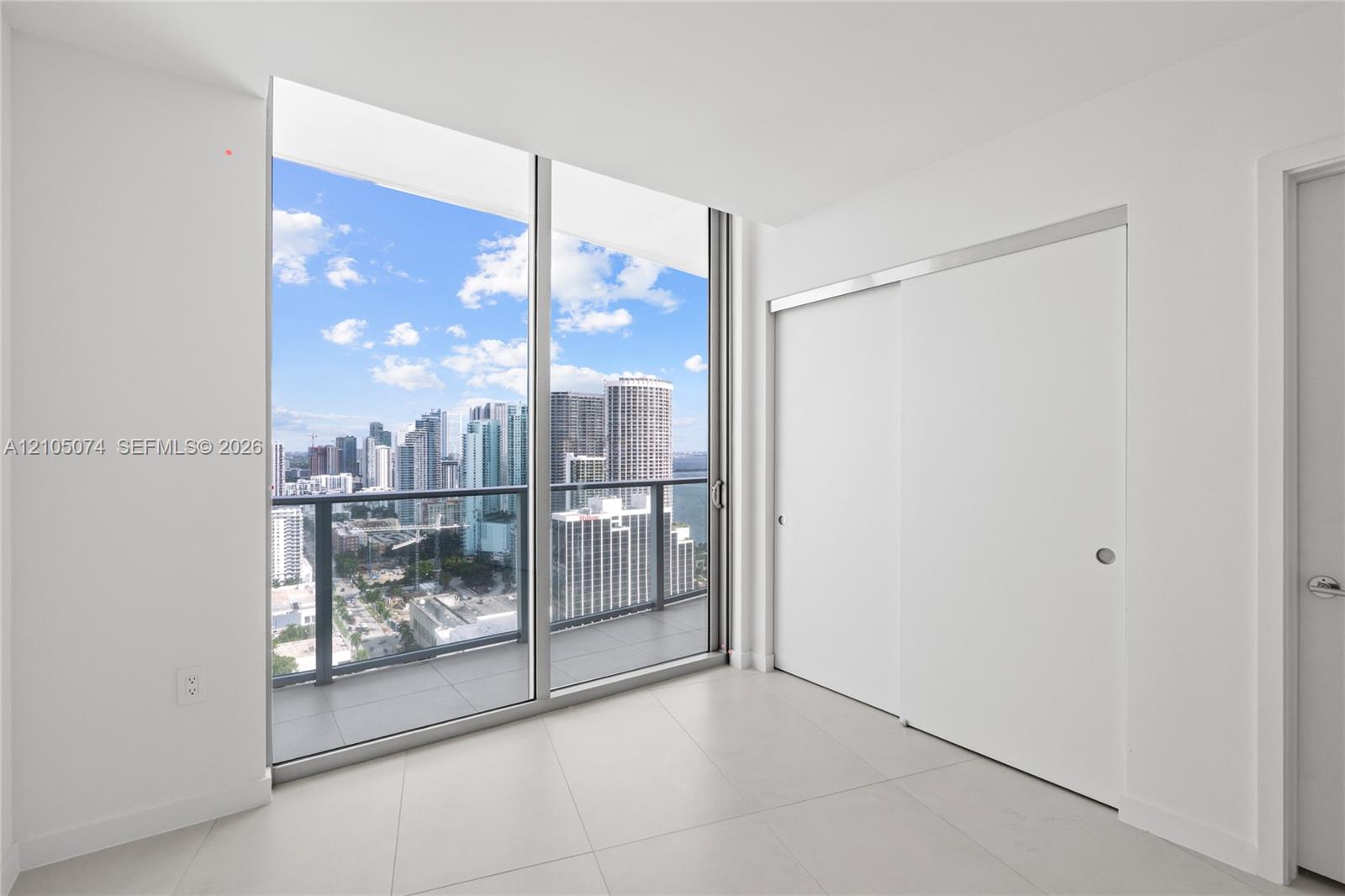 Floor-to-ceiling windows, sliding glass door, private balcony with metal railing, and large-format tile flooring