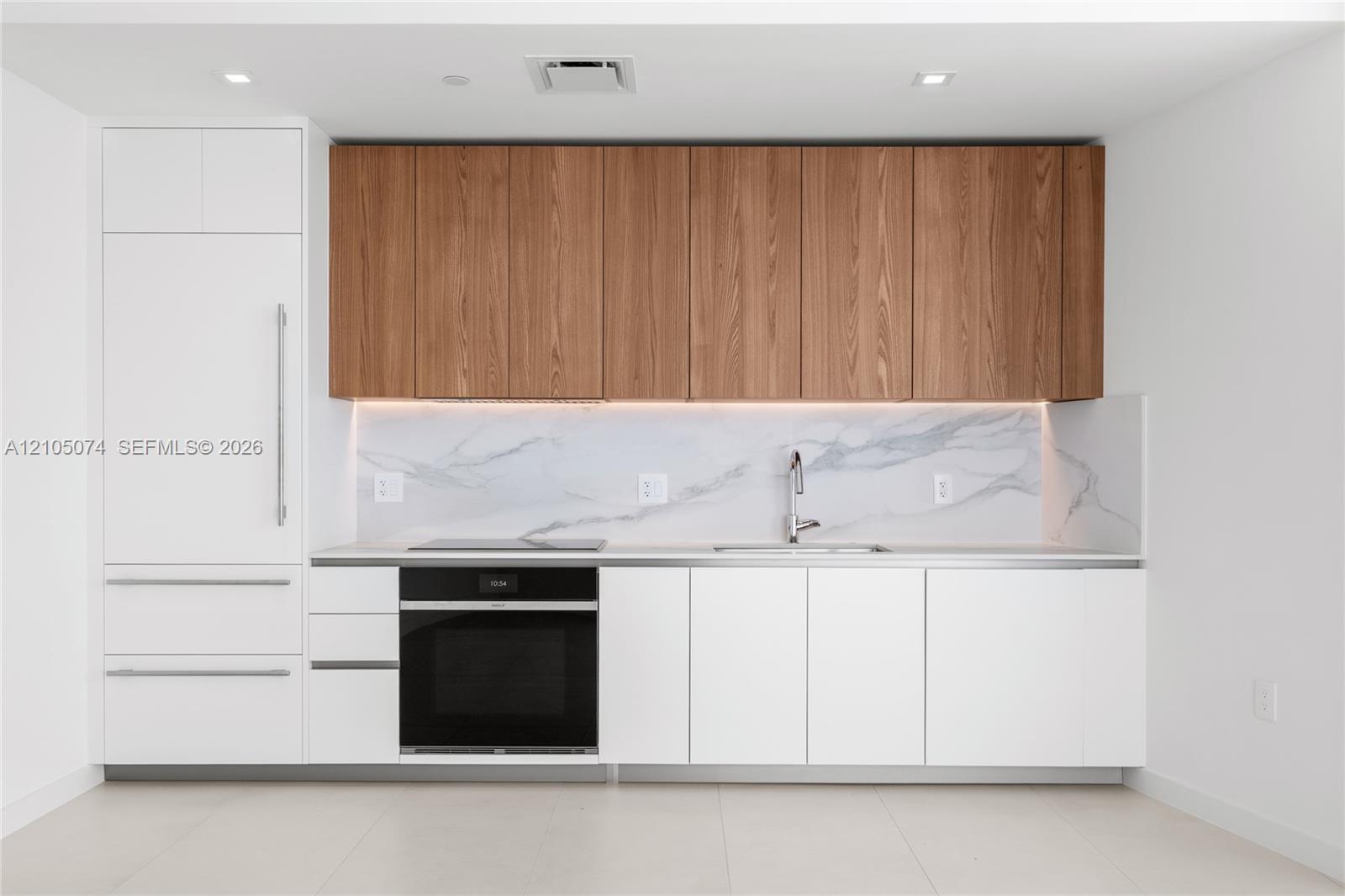 Modern kitchen featuring flat-panel white lower cabinetry, wood-finish upper cabinetry, integrated appliances, a stone-patterned backsplash, and recessed lighting