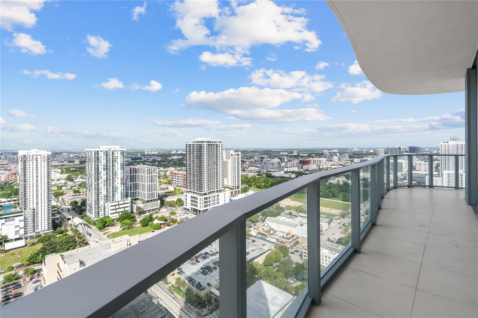 Covered balcony featuring expansive tile flooring and a glass railing system with a metal frame