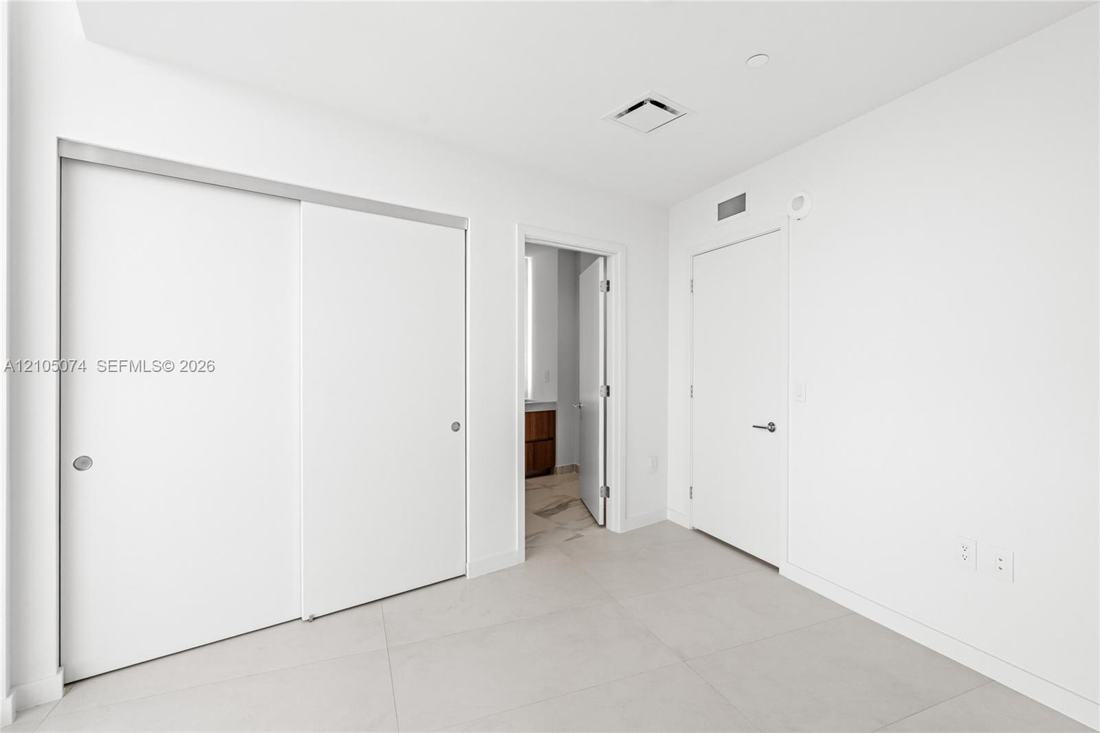 Neutral-toned large-format tile flooring, sliding closet doors, and solid-core swing door with brushed nickel hardware