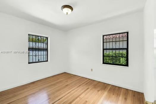 Interior space featuring wood-finish flooring, two windows with black metal security bars, and a central flush-mount ceiling light fixture