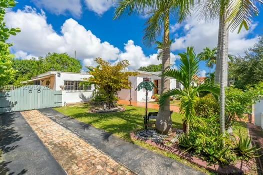 Exterior featuring a stucco facade, brick-accented driveway, decorative wood-style gate, and mature palm landscaping