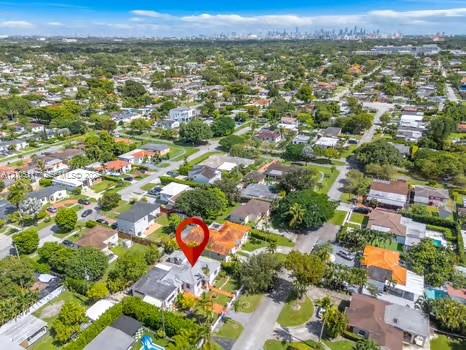Aerial perspective showcasing a residential property with a tiled roof, situated within a suburban neighborhood featuring mature canopy trees and distant metropolitan skyline