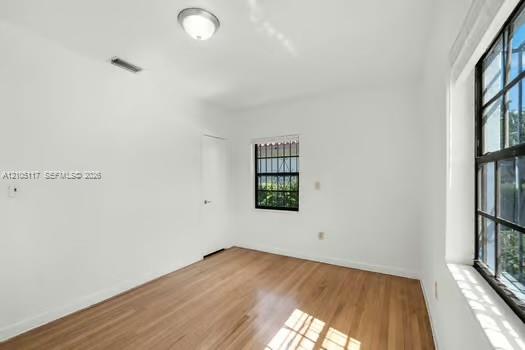 Interior room featuring wood-finish flooring, white walls, dual windows with black frames and security bars, and a central ceiling-mounted light fixture