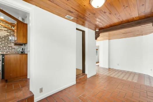 Interior space featuring tongue-and-groove wood-finish ceiling planks, terracotta-style brick flooring, and exposed brick accent wall