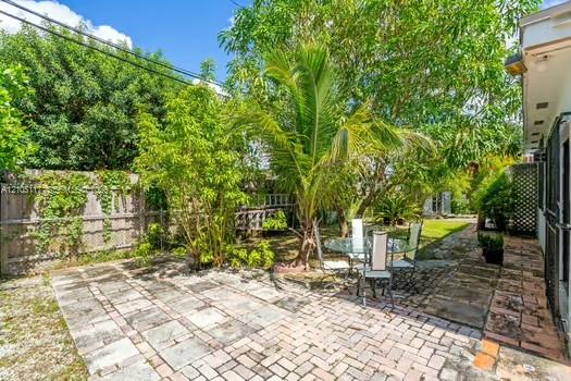 Private backyard featuring a paved stone patio, perimeter wood fencing, established tropical landscaping, and mature trees