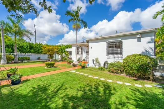Exterior grounds featuring a manicured lawn, brick-paved pathways, circular stone stepping stones, perimeter privacy fencing, and mature palm trees